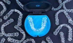 Bird’s eye view of Invisalign in carrier case surrounded by multiple trays on black surface