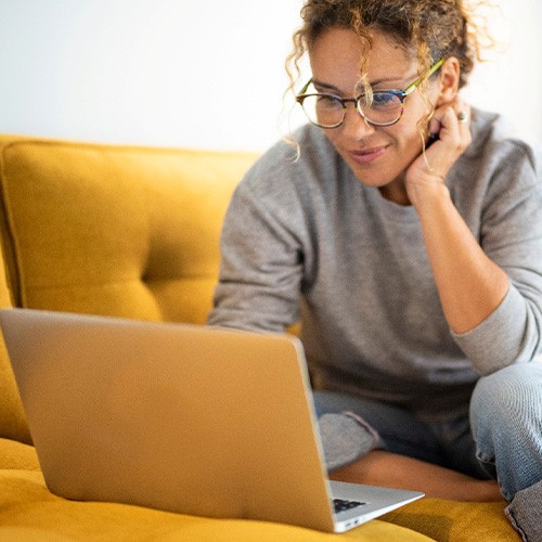 Woman smiling while working on laptop on couch
