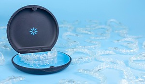 Many Invisalign trays surrounding carrier case on light blue surface