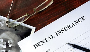 Top of dental insurance form with glasses, X-rays, money, and pen