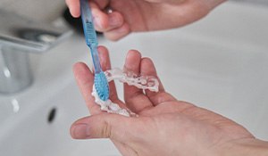 Closeup of patient cleaning clear aligner in sink