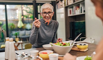 Woman with black glasses smiling while eating with friend