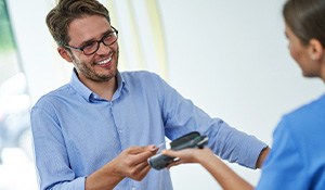 Man holding out credit card to woman with payment device at counter with model teeth