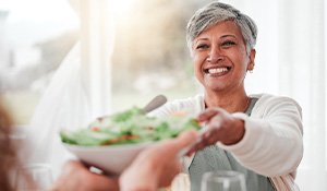 Smiling woman grabbing salad bowl across the table