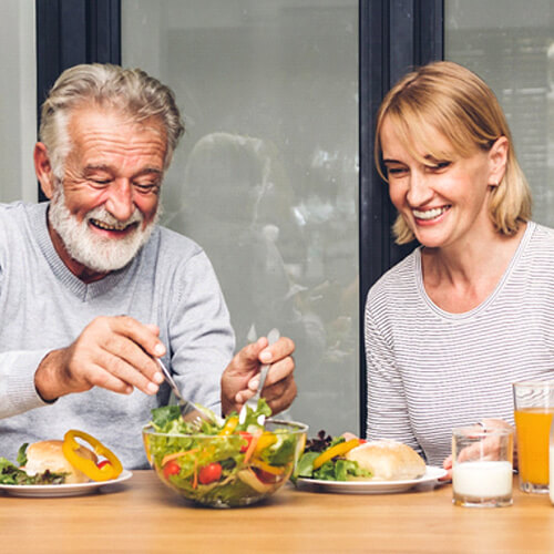An older couple seated at a table eating sandwiches and salad together