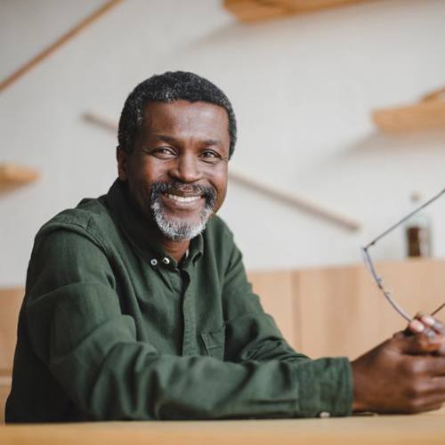 older man smiling and holding his glasses 