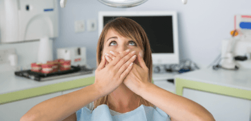 Woman in dental chair covering her mouth