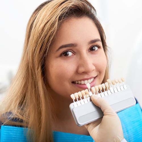 dentist holding a row of veneers up to a patient’s smile 