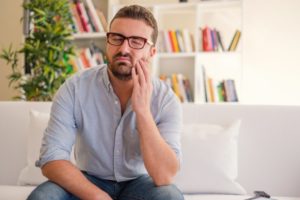 man who needs a root canal holding his cheek in pain