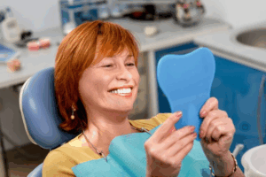 Woman with newly whitened teeth smiling in small mirror