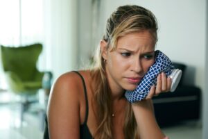Woman holding cold compress to the side of her face.